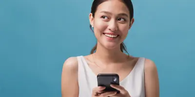 Girl holding mobile phone as she smiles looking off to the side