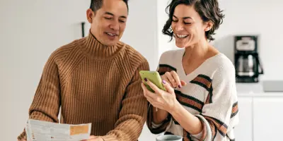 Couple standing at a table looking at their phone and laptop together