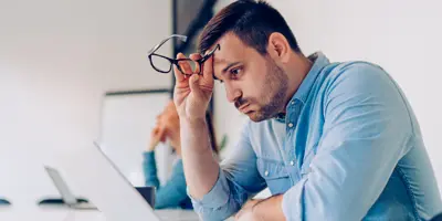 Man sitting at desk in front of his laptop looking exhausted