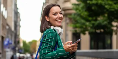 Girl in green suit jacket smiling as she holds her phone walking outside